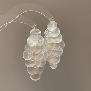 Macro detail of layered white shell drop earrings with golden hooks and pearl-like luster