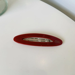 Detailed view of red oval hair clip with gold France Handmade lettering on white background