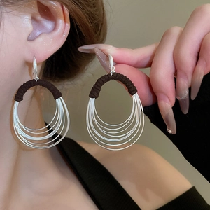 Close-up of dangling silver multi-hoop earrings with dark braided cords on model