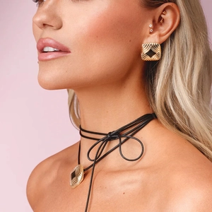 Detail of square gold earrings and black cord necklace worn on a fashion model
