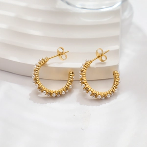 Macro detail of 18k gold plated C-shaped earrings with inlaid pearls on a textured stand