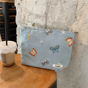 Detail of embroidered butterflies and white flowers on a light blue fabric makeup bag