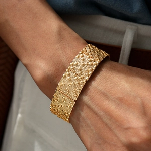 Gros plan d'un large bracelet doré avec surface texturée en relief et finition métal vintage