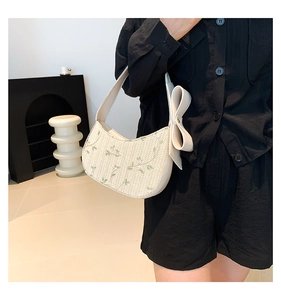 Close-up of floral embroidery and cream bow detail on woven straw shoulder bag