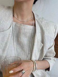Detail of a long silver snake chain necklace styled with a minimalist gray linen suit