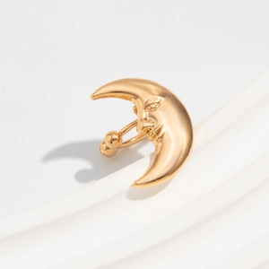 Macro view of a gold metallic celestial moon face earring on a textured white pedestal
