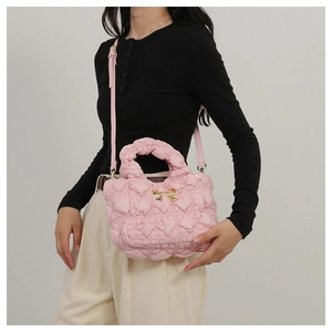 Detail of pink quilted puff handbag with gold bow charm and shoulder strap on model