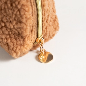 Close-up of golden metal zipper and plush teddy fabric texture on makeup bag