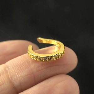 Close-up of gold-plated ear cuff with pavé zircon stones on a dark background