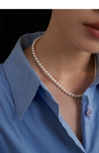 Close-up of elegant white pearl necklace on model in blue shirt showing lustrous round beads