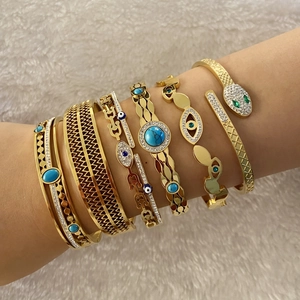 Detailed view of stacked gold bracelets featuring turquoise, evil eye and snake head motifs