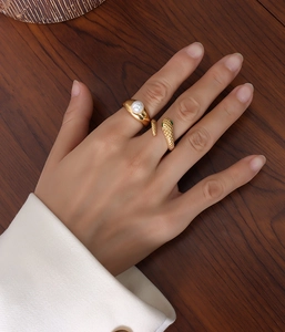 Detail of 18k gold plated snake ring with green stone and pearl ring on hand