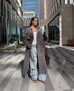 Détail du trench-coat en daim gris foncé avec un jean large bleu clair à effet usé