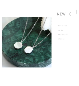 Detail of silver geometric pendants on green marble texture stand for a minimalist style
