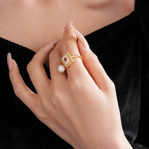 Detail of gold-plated square pendant ring with pearl and red gemstone on a finger