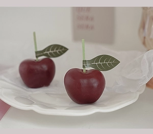 Primer plano de velas aromáticas con forma de cereza y etiqueta de hoja