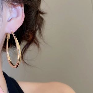 Close-up of elegant large golden resin hoop earring worn by a model for a luxury look