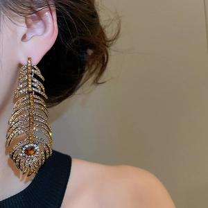 Close-up of luxury feather earrings with amber rhinestones on gold metal base