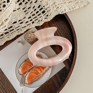 French handmade oval hair claw clip with pink and white stripes on a wooden tray