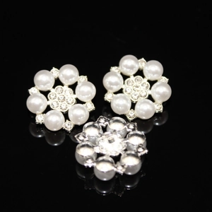 Macro detail of three flower-shaped pearl and rhinestone alloy buttons on black mirror