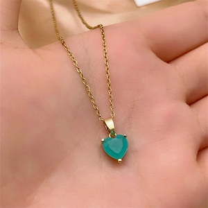 Close-up of heart-shaped green gemstone pendant on golden necklace held in hand