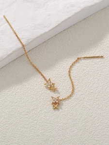 Detailed close-up of golden tassel earrings with star zircon elements on stone background