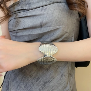 Detail of silver open cuff bracelet with shell texture on model's wrist with soft lighting