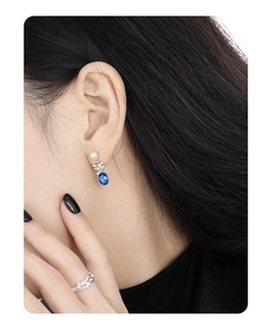 Close-up of pearl earrings with blue gems and a silver hollow design textured ring