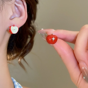 Detailed view of asymmetric red apple studs with enamel finish and small crystal accents