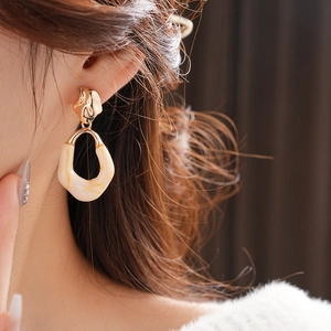 Close-up of golden irregular metal earrings with cream resin inlay worn by a model