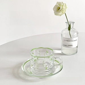 Detailed view of glass cup and saucer set with lily of the valley floral pattern