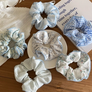Set of six floral and polka dot fabric scrunchies with blue ruffled edges on a wooden table