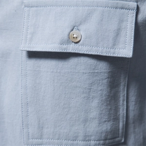 Detailed macro view of the chest pocket and button on a light blue cotton shirt