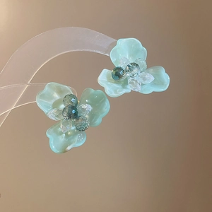 Elegant mint green flower stud earrings with beaded center hanging on a clear display
