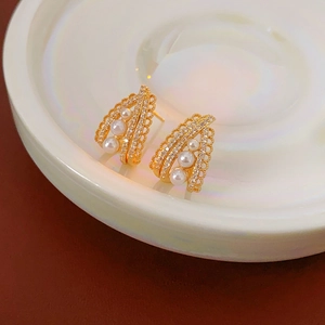 Detail of gold pearl and zircon flower earrings on a white ceramic plate tray