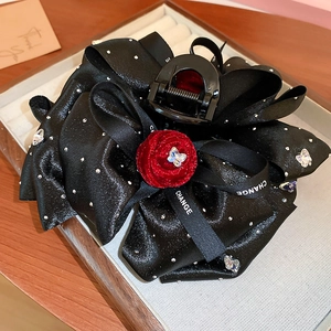 Macro detail of black satin bow hair claw with red velvet rose and crystal butterfly