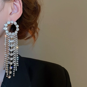 Close-up of sparkling silver tassel earrings with round studs on a model in a black suit