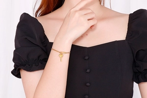 Détail d'un bracelet doré avec pendentif clé en cœur porté au poignet, chaîne réglable
