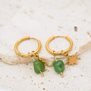 Macro shot of gold-plated star charms and green natural stones on rock texture