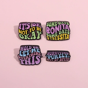 Detailed macro view of four colorful enamel pins with creative English quotes on pink background