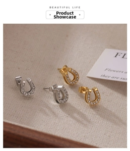 Detailed view of gold and silver horseshoe earrings with zircon inlay on textured fabric