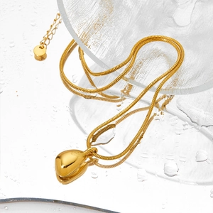 Polished gold snake chain necklace with geometric teardrop pendant on glass surface