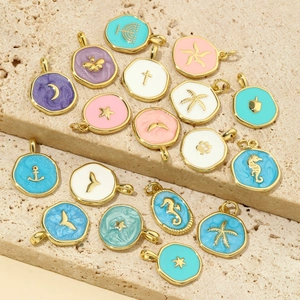 Assorted ocean theme macaron enamel pendants in gold-plated alloy on marble