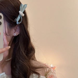 Detail of light blue satin bow hair clip with white pearls on model's wavy brown hair