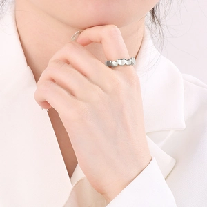 Close-up of heart-shaped linked stainless steel ring on model's finger with silver finish