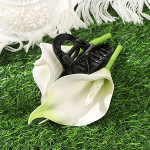 Close-up of white calla lily hair claw clip with green stem handle on green grass