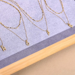 Detail of double-layer gold necklaces with HOPE letter pendants on purple velvet