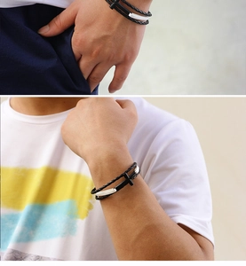 Close-up of black braided leather bracelet featuring silver metal cross and bar details