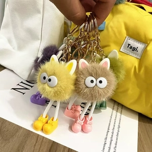 Cartoon fuzzy puff ball keychain with long legs and colorful boots on a stylish handbag