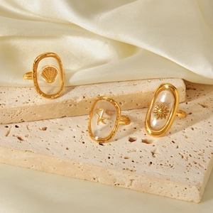 Detailed shot of three gold rings with shell, starfish, and sun icons on stone and silk